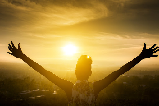 girl with arms raised wide in front of the sun set